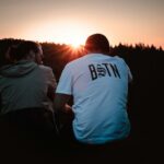 man in white crew neck t-shirt standing beside woman in black jacket during sunset