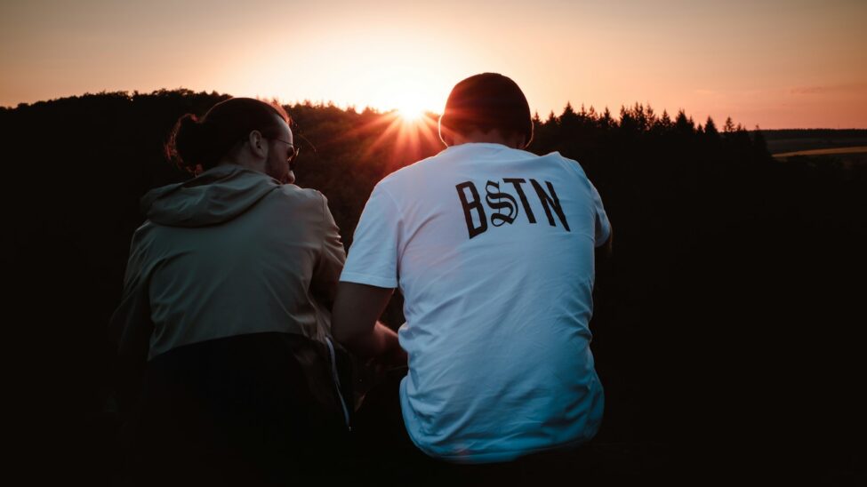 man in white crew neck t-shirt standing beside woman in black jacket during sunset